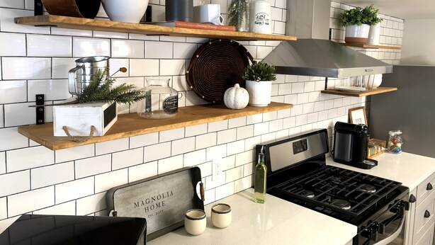 A kitchen with white tiled backsplash, wooden shelves, and various kitchen items.