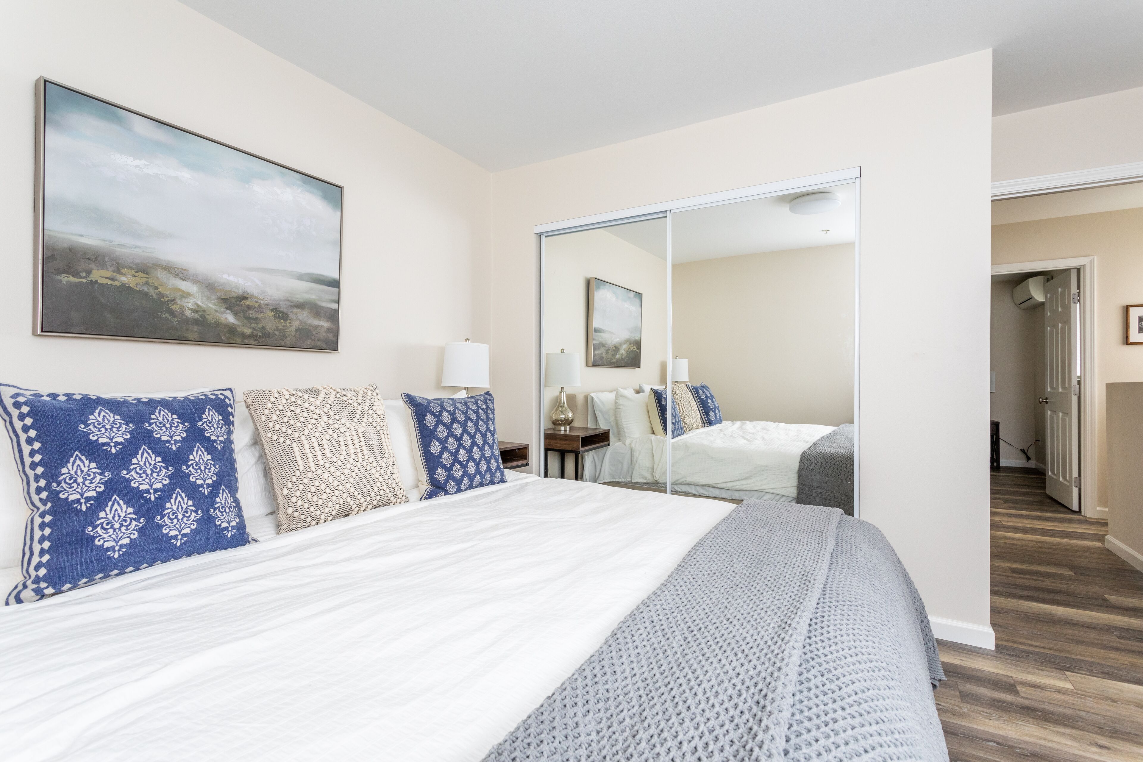 A bedroom with a large bed, a mirror, and a painting on the wall.