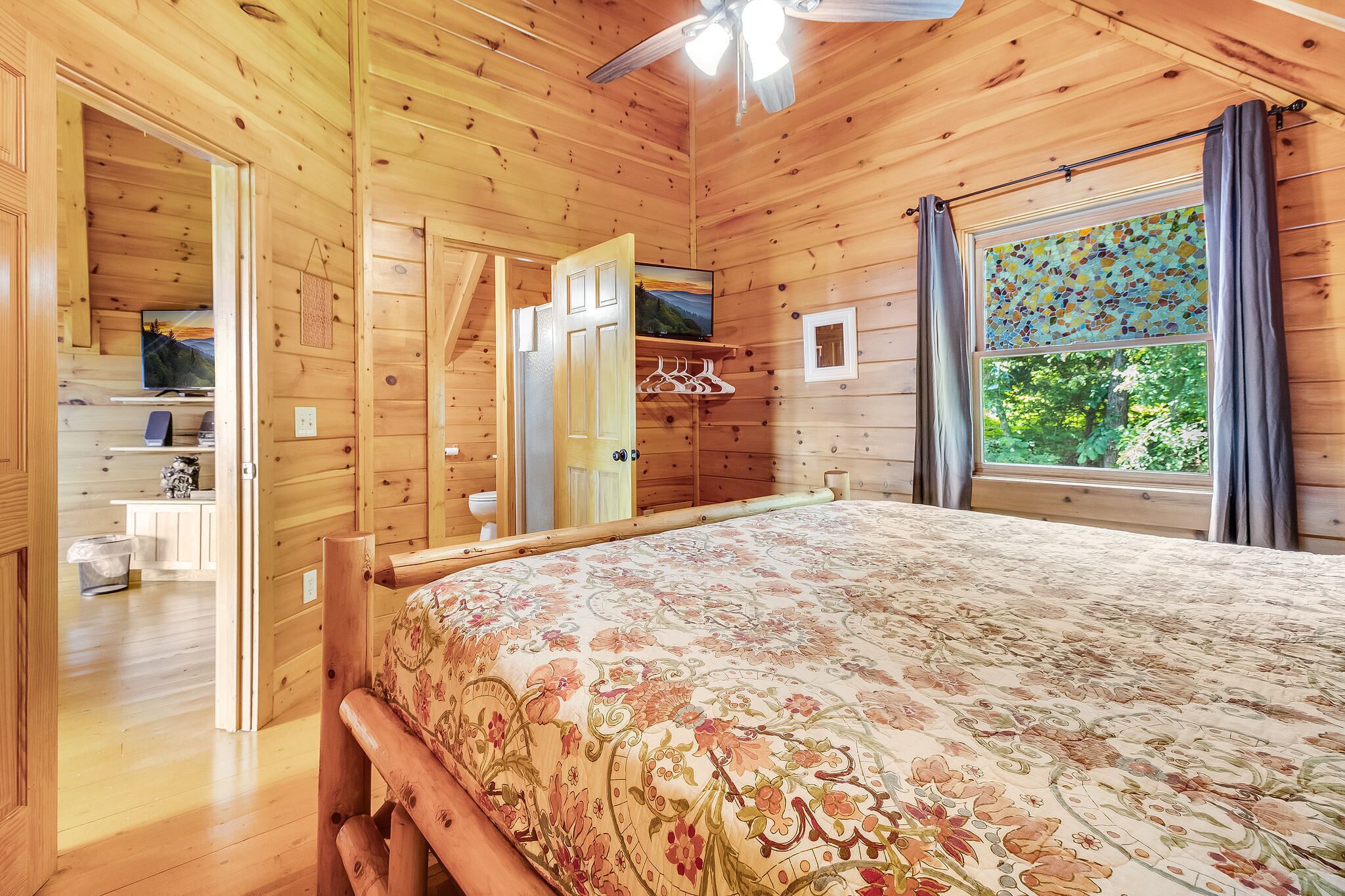 Un dormitorio de cabaña de madera con cama, televisor y ventana con cortinas.