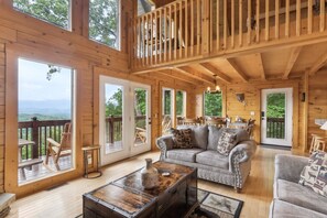 A spacious wooden cabin with a loft bedroom, a cozy living area with a sofa and coffee table, and large windows offering scenic views. - Bearhemain Rhapsody, a Private Cabin with Incredible Mountain Views, Near Dollywood!! (Sevierville)
