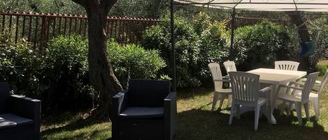 Un patio al aire libre con mobiliario de mimbre, una mesa y sillas bajo un toldo.
