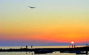 A sunset over a calm body of water with boats and people on the shore.