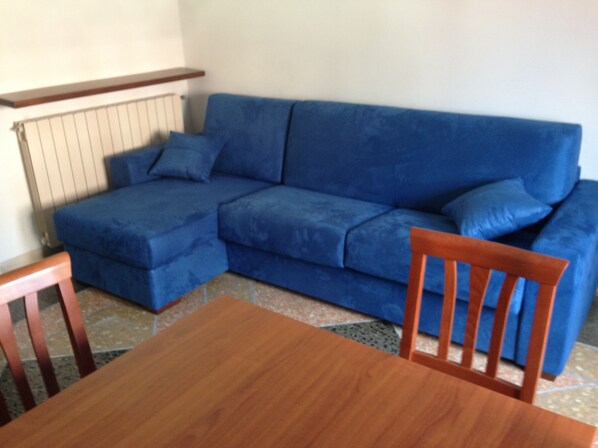 A blue sofa with wooden legs, a wooden table, and a chair.
