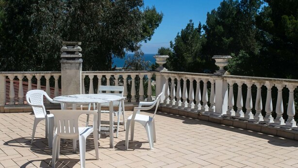 Un patio al aire libre con una mesa y sillas, una barandilla y vista al mar.