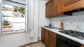 Una cocina con armarios de madera, estufa a gas, pileta y ventana con vista a un edificio y una escalera.