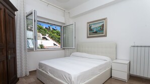 Un dormitorio con una cama, una mesita de noche, una ventana con cortinas, un radiador y un cuadro en la pared.