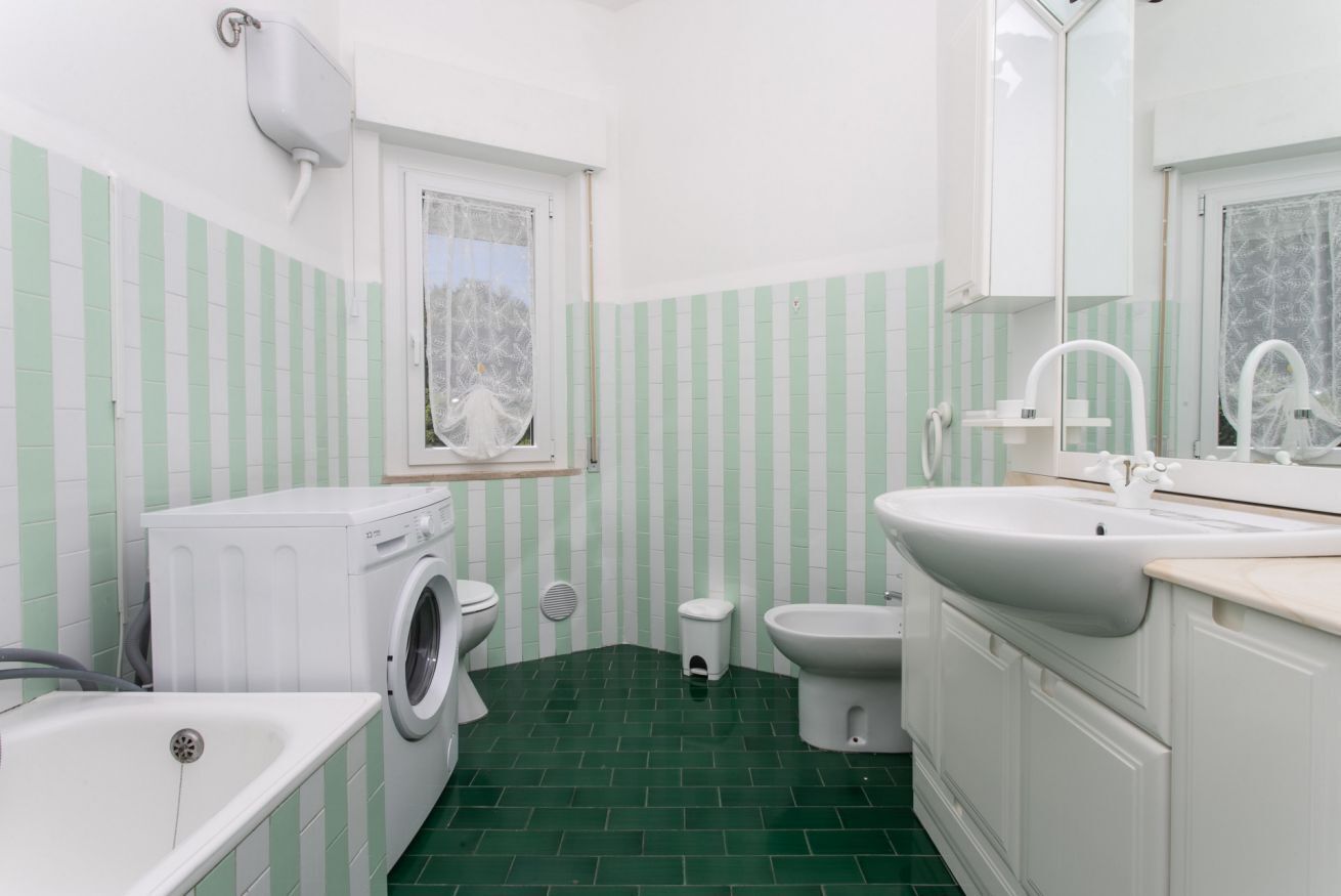 A compact bathroom with a washing machine, toilet, sink, and a small window.