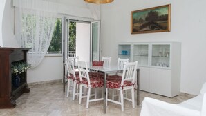 Un comedor con mesa y sillas blancas, un cuadro en la pared y un mueble con puertas de vidrio.