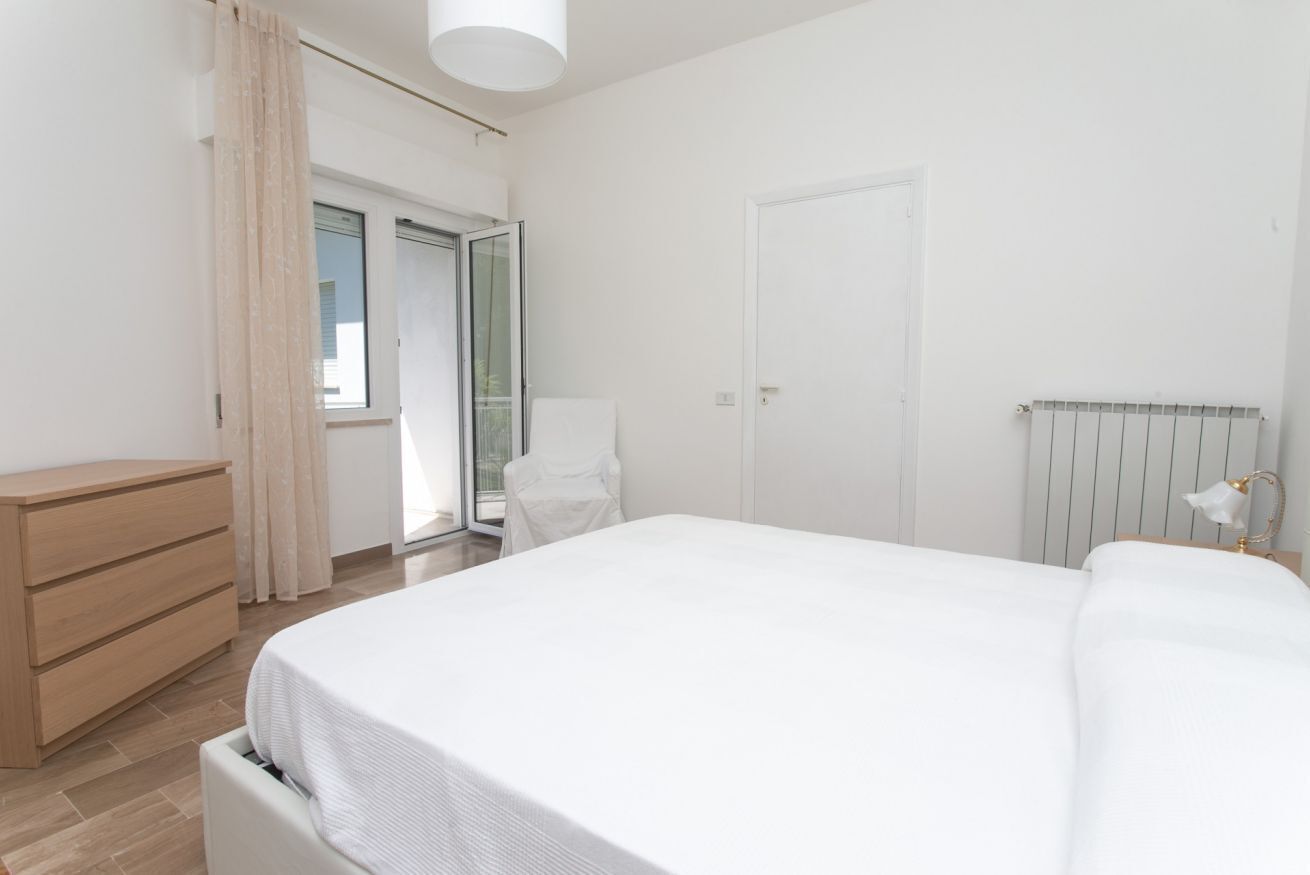 A bedroom with a bed, a dresser, a chair, a radiator, and a door.