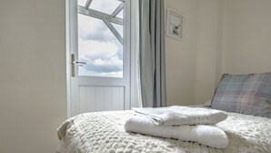 A bedroom with a large window, a bed with a white blanket, and a plaid pillow.