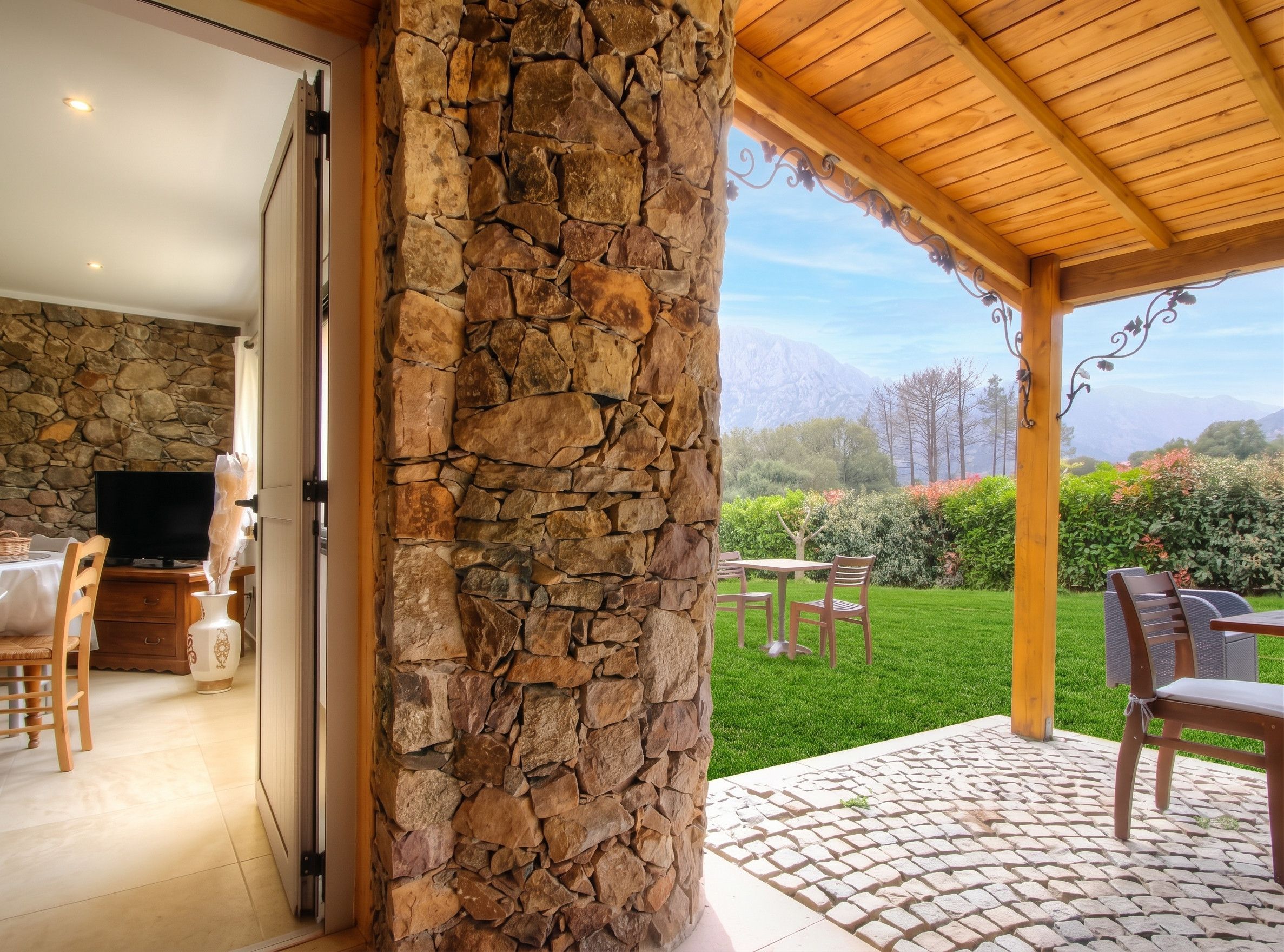 Un muro de piedra, una pérgola de madera y vistas a un paisaje montañoso.