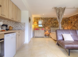 A compact living space with a kitchenette, a stone wall, a bed, and a leather sofa.