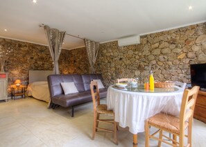 Une pièce chaleureuse avec un mur en pierre, un canapé, une table à manger avec des chaises et un téléviseur.