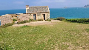 A stone cottage with a small porch, a grassy area in front, and a view of the sea. - Homerez - House in Saint-Alban (Saint-Alban)