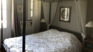 Quarto com uma cama de dossel, mesa de cabeceira com abajur e um quadro na parede.