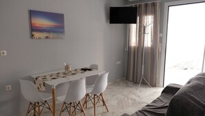 Un coin repas avec une table et des chaises, un téléviseur à écran plat fixé au mur et une grande fenêtre avec des rideaux.