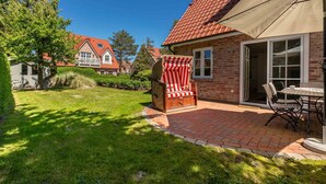 Eine Terrasse mit Ziegelboden, einem gestreiften Gartenstuhl und einem Tisch mit Stühlen.