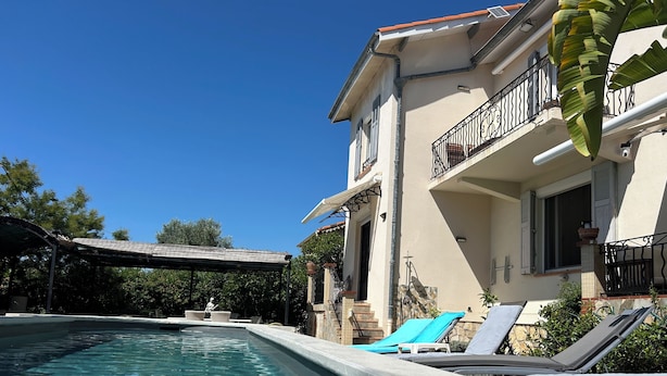 Una piscina con sillas de descanso, un porche cubierto y un edificio con balcón.