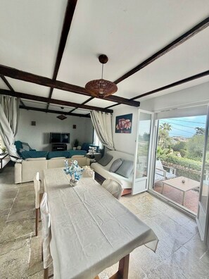 A spacious living area with a sofa, dining table, and a large window offering a view of the outdoors.