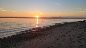 A beach at sunset with a clear sky, calm water, and a person rowing a boat.