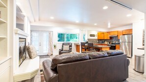A modern living room with a leather sofa, a dining area with a small table and chairs, and a kitchen with wooden cabinets and stainless steel appliances.
