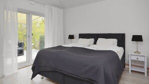 A bedroom with a bed, two bedside tables, a nightstand, and a sliding glass door leading to a balcony.