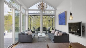 A spacious living room with a large glass door leading to an outdoor area, a modern chandelier, and a large painting on the wall.