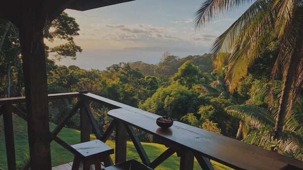 A wooden deck with a table and stools overlooking a lush landscape.