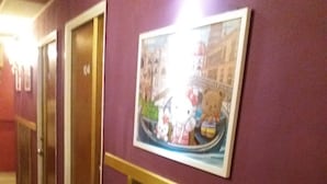 Un pasillo con puertas numeradas 104 y 105, un cuadro enmarcado con personajes de Hello Kitty y un suelo de mármol.