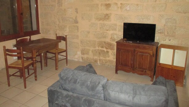Sala de estar com parede de pedra, mesa de jantar de madeira com cadeiras, sofá cinza e televisão sobre um armário de madeira.
