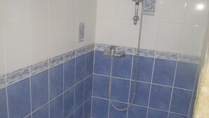 Casa de banho com azulejos azuis e brancos, chuveiro com chuveiro manual e uma pequena janela.