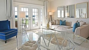 A modern living room with a blue sofa, beige sofa, and a glass coffee table. There are two chairs with cushions, a lamp, and a ceiling fan. - Style, Luxury & Stunning Views (Reunion)