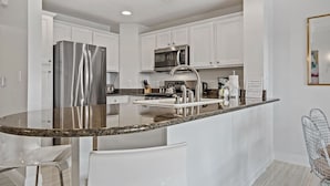 A modern kitchen with white cabinetry, stainless steel appliances, and a granite countertop island. - Style, Luxury & Stunning Views (Reunion)