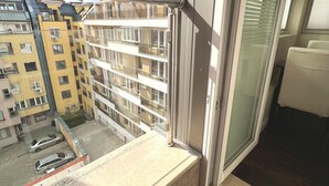 Un balcón con vista a un edificio de varios pisos, una puerta de cristal y piso de baldosas.