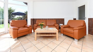 Un salon moderne avec deux canapés en cuir, une table basse en bois et une grande porte-fenêtre coulissante donnant sur un espace extérieur équipé d’un parasol.