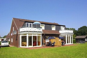 Ein zweigeschossiges Haus mit einer großen Terrasse, einer Satellitenschüssel und einem überdachten Sitzbereich im Freien.
