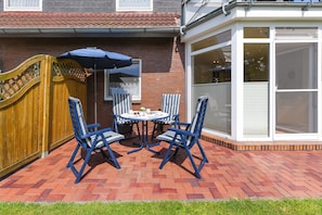 Eine Terrasse im Freien mit Backsteinpflasterung, Holzlattenzaun und einem überdachten Tisch mit Stühlen.