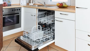 Une cuisine moderne avec des meubles en bois, un four encastré, un lave-vaisselle et une fenêtre donnant sur un mur de briques.
