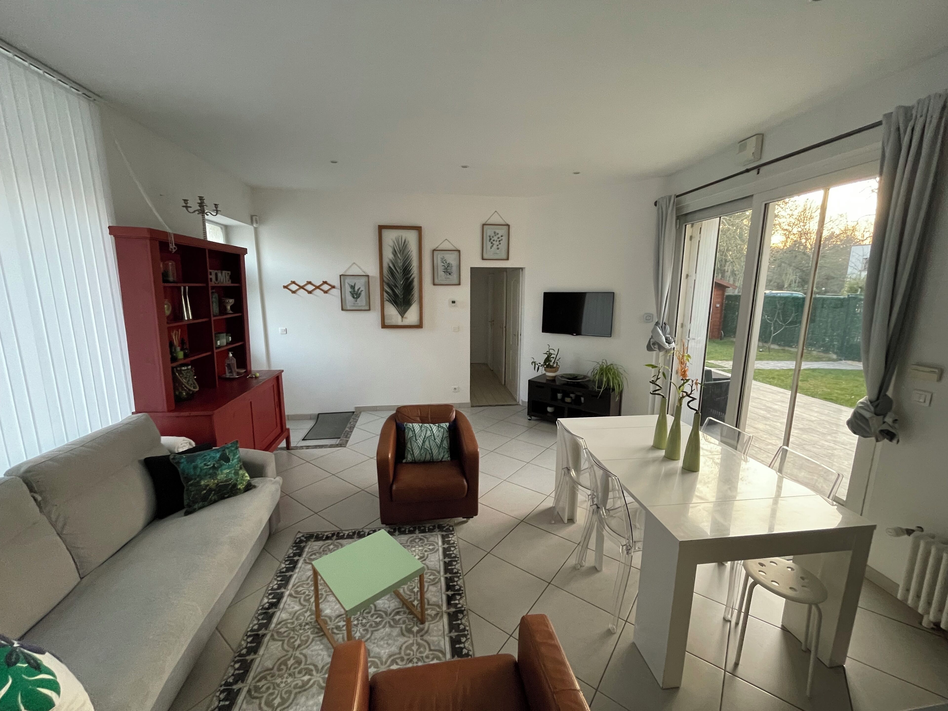 Uma sala de estar com sofá, uma poltrona marrom, mesa de jantar e televisão.
