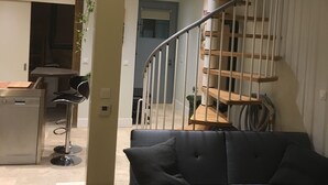 Una sala de estar moderna con un sofá azul oscuro, una mesa de centro de madera y una escalera en espiral con barandilla de metal.