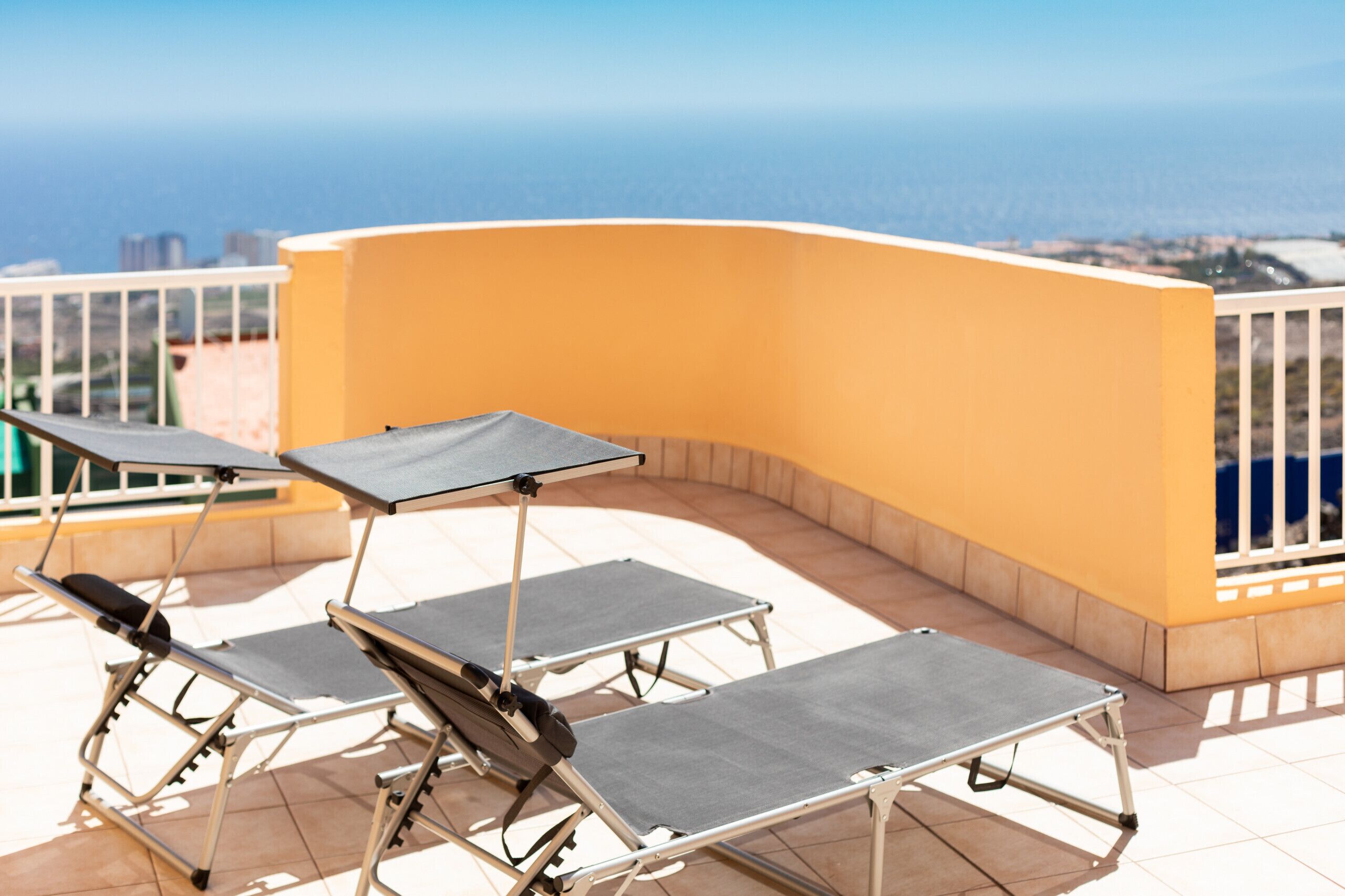 Une terrasse avec trois chaises longues et une table, offrant une vue sur la côte.