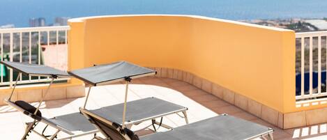 Une terrasse avec trois chaises longues et une table, offrant une vue sur la côte.