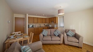 A compact living space with a kitchenette, a dining area, and two sofas with striped cushions. - Location Location! Spacious 2 Bed Apt Hastings - Country & Sea Views (Hastings)