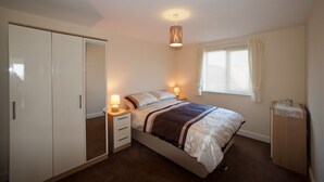 A bedroom with a bed, bedside tables, a wardrobe, a window with curtains, and a ceiling light fixture. - Location Location! Spacious 2 Bed Apt Hastings - Country & Sea Views (Hastings)