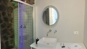 Un baño con un lavabo blanco, un espejo redondo y una ducha con pared de azulejos.