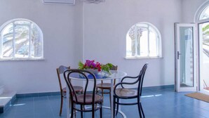 Un comedor con una mesa redonda, cuatro sillas y un jarrón de flores. Hay dos ventanas con arcos y una puerta con paneles de vidrio.