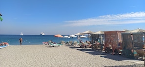 Una playa con tumbonas, sombrillas y un velero a lo lejos.