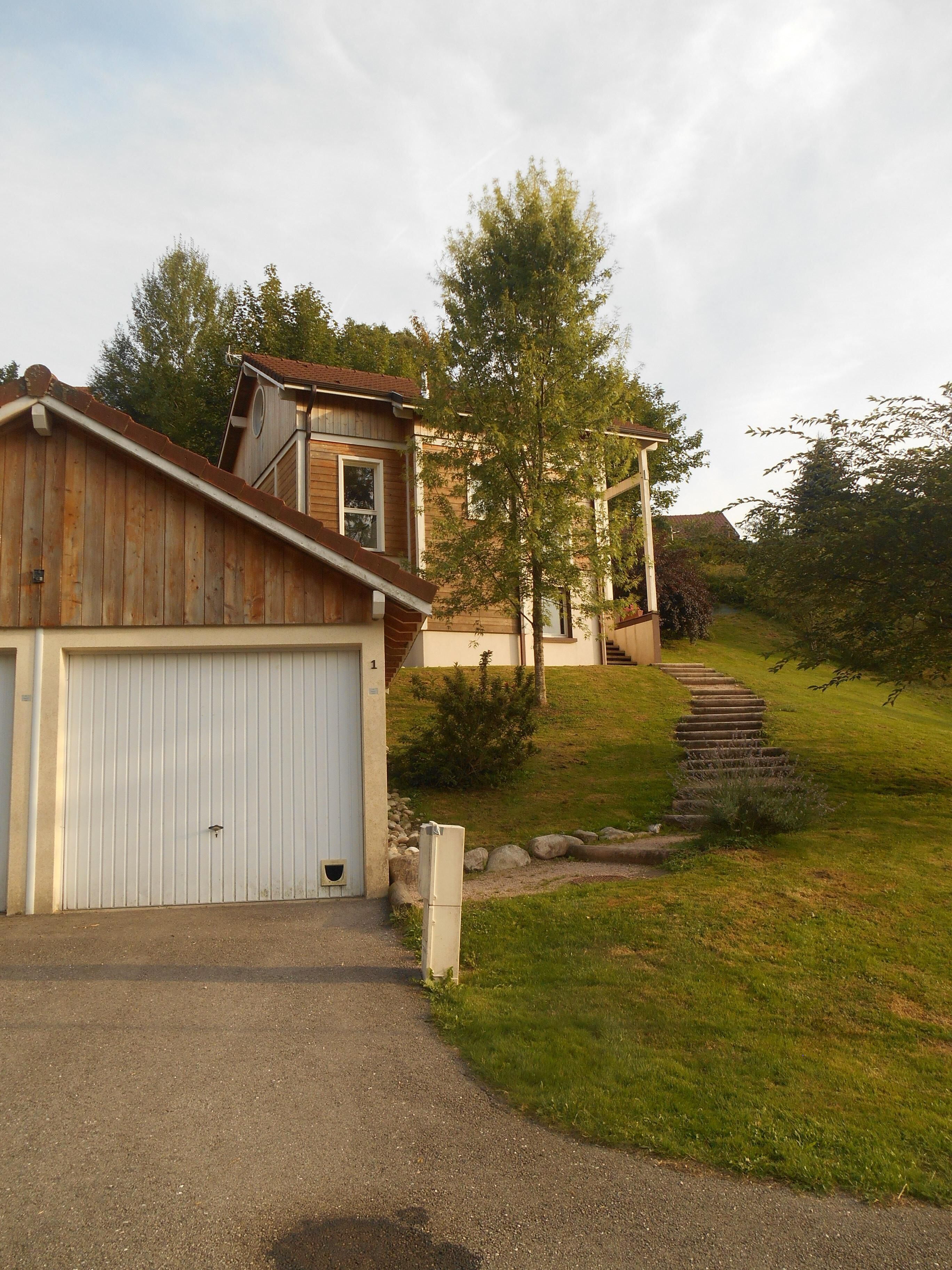 A residential property with a garage, a wooden house, and a staircase leading to a second-floor balcony.