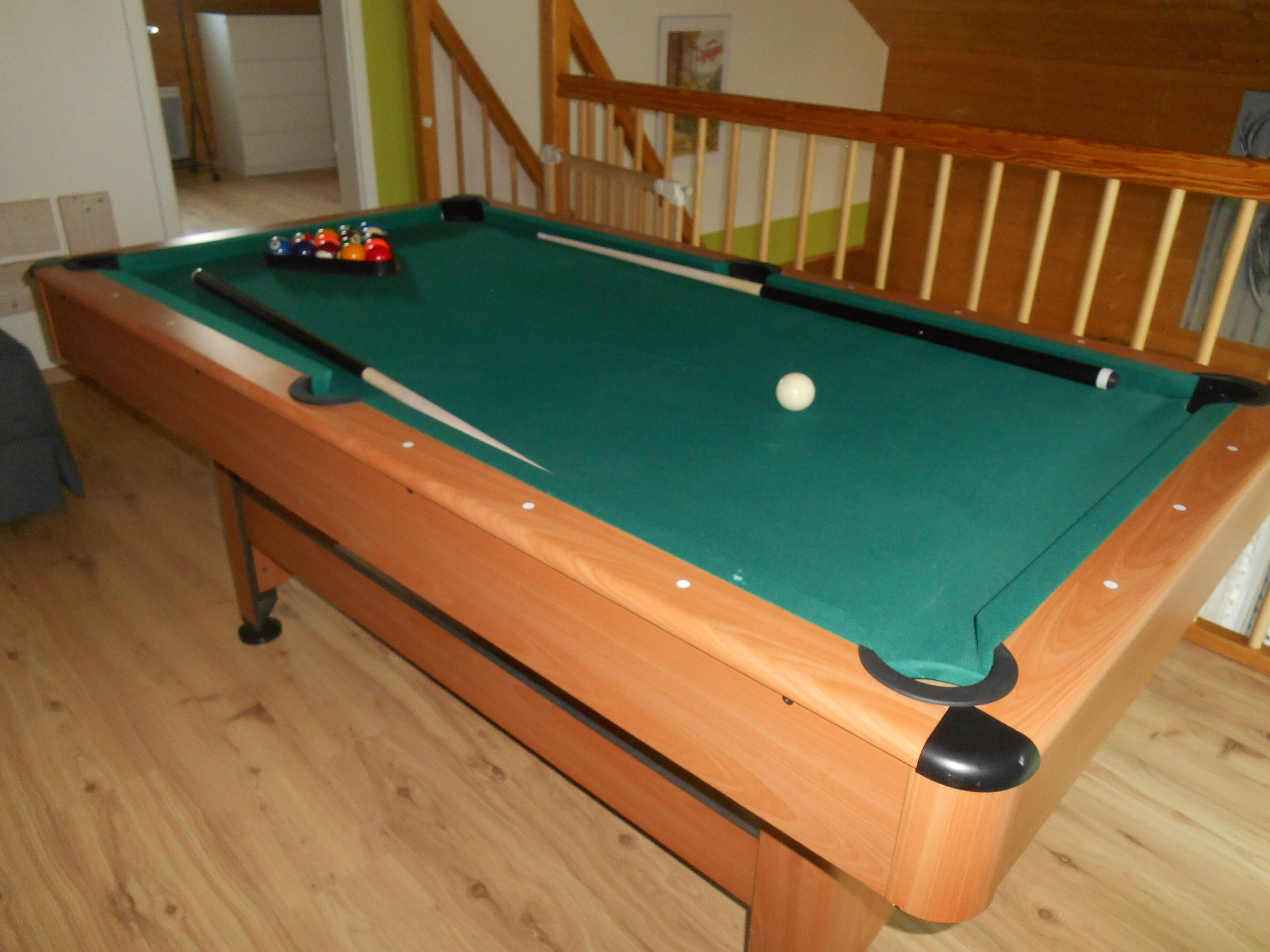 Una mesa de billar con bolas, una superficie de fieltro verde y una mesa de madera.