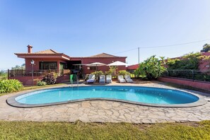 A house with a swimming pool, a covered patio with lounge chairs, and a garden.